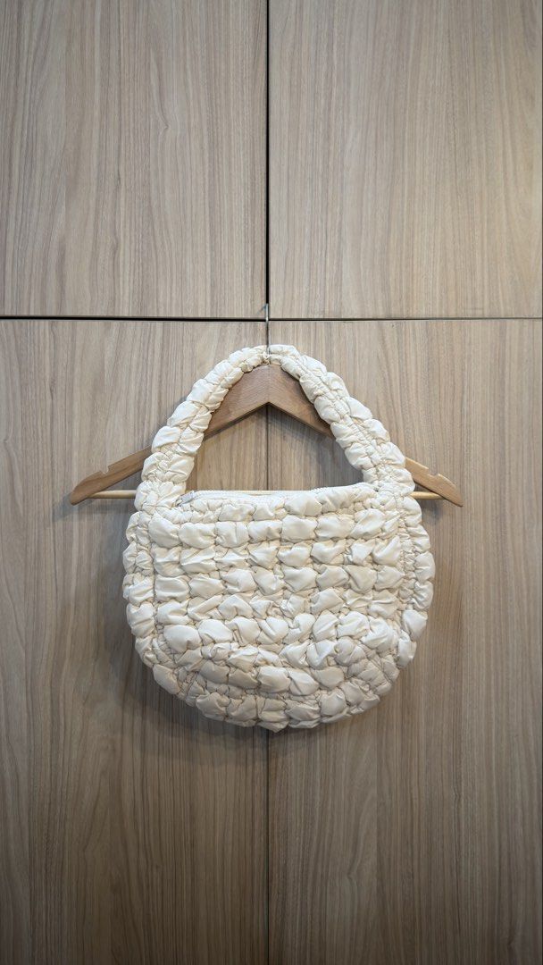 COS quilted Mini Bag (Category: Luxury Bags & Wallets) located in Alfonso. Submitted by jbcamet (Listing ID 1426297331, Image 1). Description: Cream-colored mini bag from COS. Features a quilted design and a top handle. The bag has a zipper closure. The interior has a COS label. The bag is hanging on a wooden hanger..