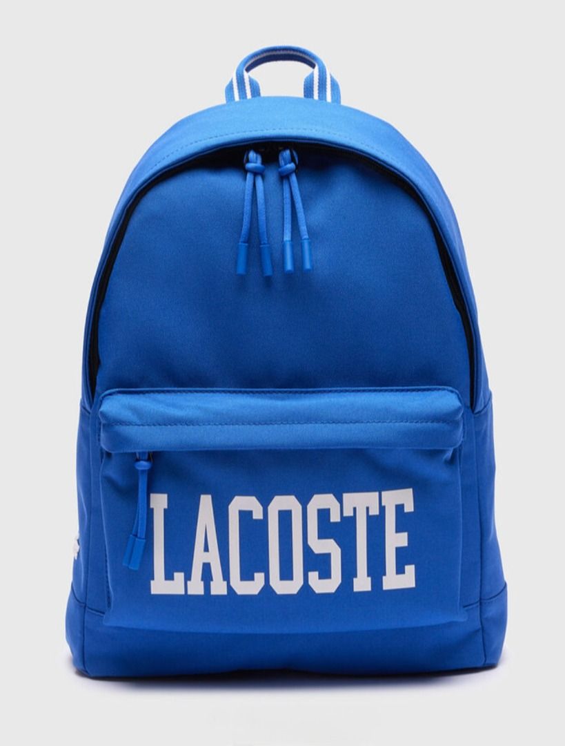 Lacoste Blue Backpack (Category: Backpacks) located in Quezon City. Submitted by henryan95 (Listing ID 1426277748, Image 1). Description: Lacoste backpack is a vibrant blue color. It features the Lacoste logo prominently displayed on the front pocket. The backpack has a top handle and two shoulder straps. The zippers have blue pull tabs. The backpack is a classic design, suitable for everyday use..