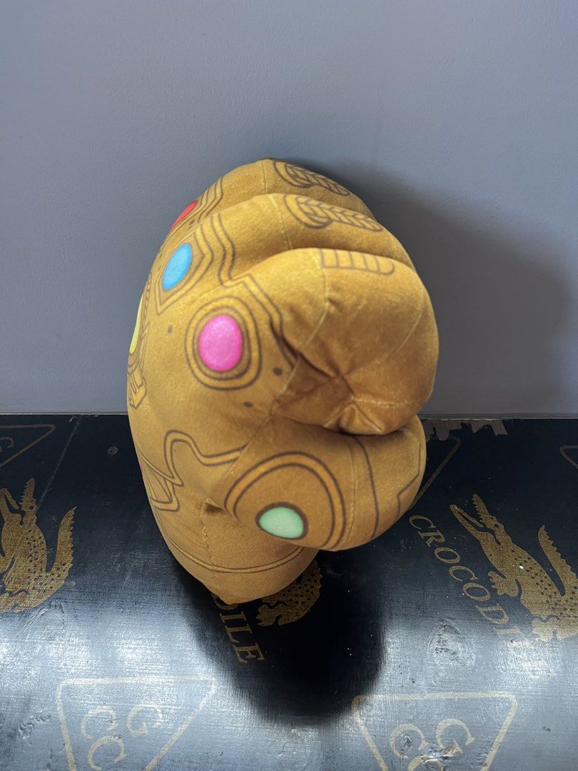 Marvel Thanos Infinity Gauntlet Plush (Category: Plushies & Soft Toys) located in Cabiao. Submitted by ronangeloo (Listing ID 1426238091, Image 3). Description: Plush toy is designed as the Infinity Gauntlet from Marvel's Thanos. It features the iconic golden color and the six Infinity Stones. The Marvel logo is visible on the front. It is made in China. This plush toy is perfect for Marvel fans and collectors..