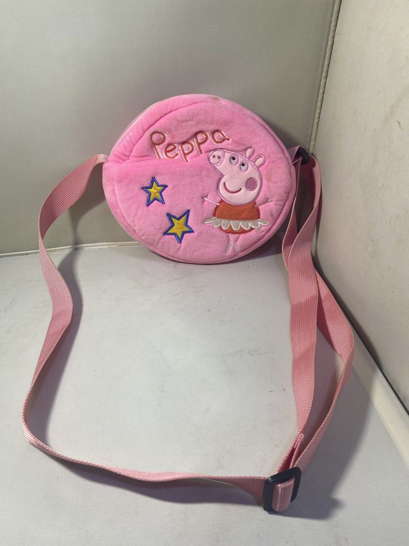 Peppa Pig Round Sling Bag (Category: Cross-body Bags) located in Pasacao. Submitted by wengpullar37205 (Listing ID 1426245762, Image 1). Description: Pink Peppa Pig sling bag features a round shape with a Peppa Pig design on the front. It has a pink strap and a zipper closure. The interior is white. The bag has some stains on the exterior. The tag inside shows the Peppa Pig logo. -need wash lng po,pro no flaw.