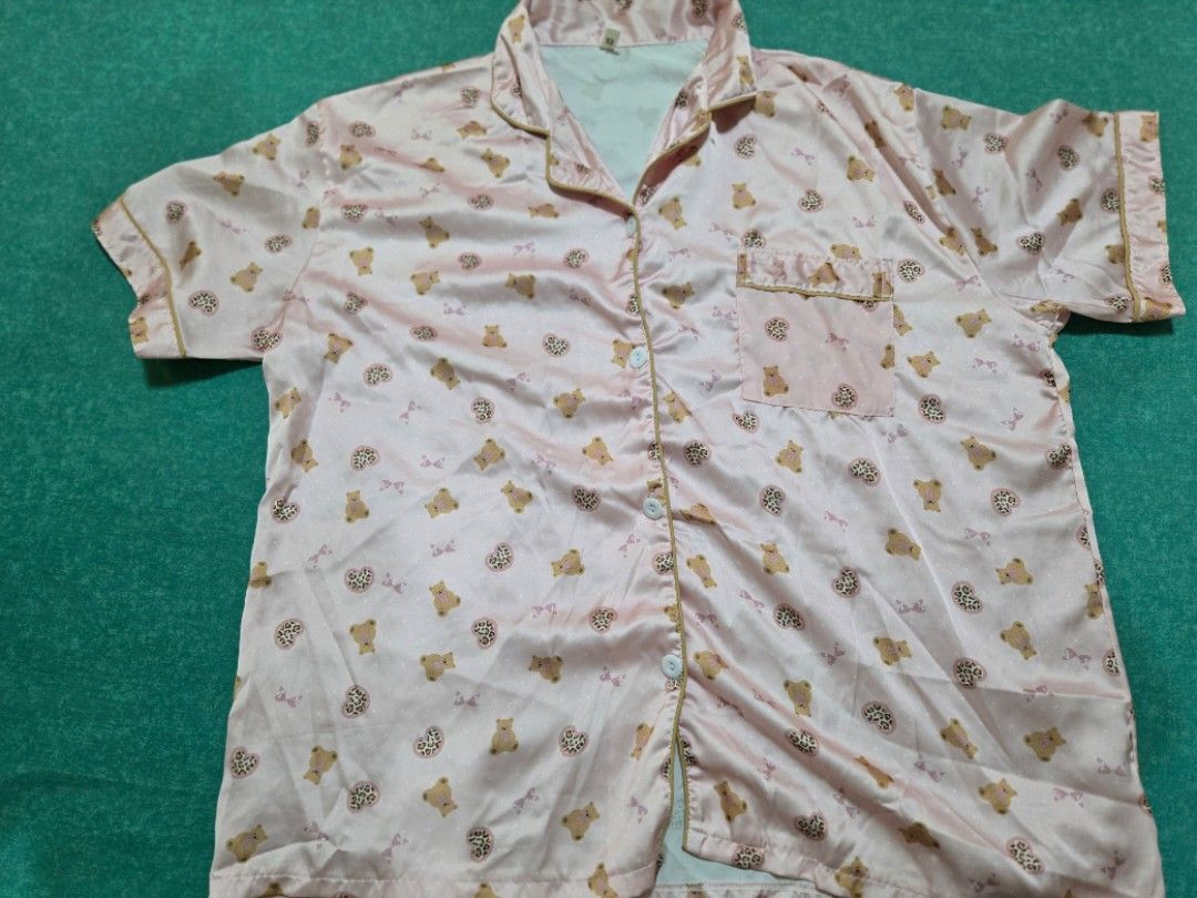 Pink Satin Pajama Set with Bear Print (Category: Undergarments & Loungewear) located in Cavite. Submitted by yogamutt (Listing ID 1426300467, Image 2). Description: Pajama set features a light pink satin fabric adorned with a cute bear print. The set includes a button-down shirt with a chest pocket and matching pants. The shirt has short sleeves and a collared neckline. The pants have an elastic waistband for a comfortable fit. Perfect for a cozy