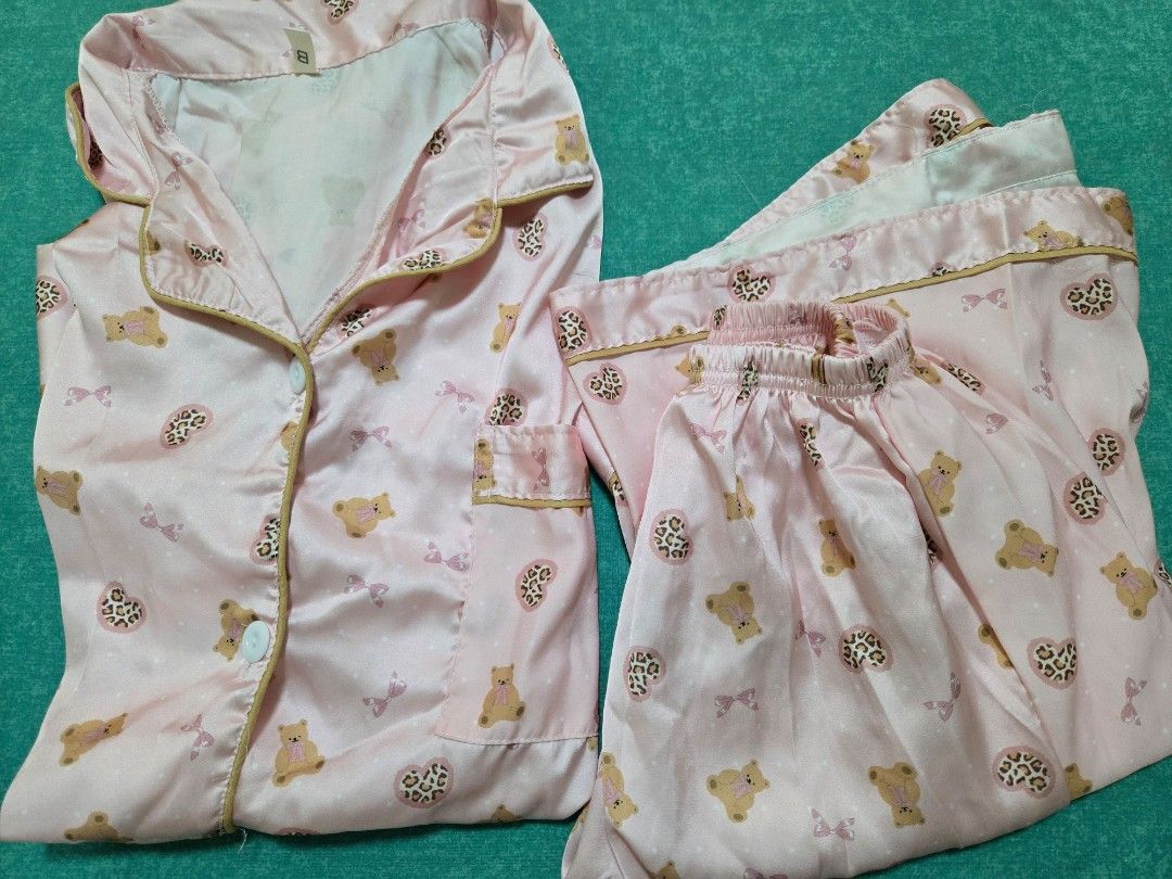 Pink Satin Pajama Set with Bear Print (Category: Undergarments & Loungewear) located in Cavite. Submitted by yogamutt (Listing ID 1426300467, Image 1). Description: Pajama set features a light pink satin fabric adorned with a cute bear print. The set includes a button-down shirt with a chest pocket and matching pants. The shirt has short sleeves and a collared neckline. The pants have an elastic waistband for a comfortable fit. Perfect for a cozy