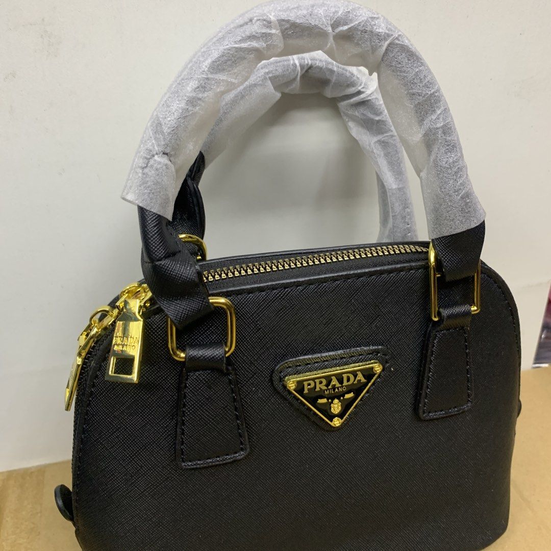 Prada Mini Dome Handbag bag (Category: Luxury Bags & Wallets) located in Pasig City. Submitted by paymelikelandlord (Listing ID 1426342224, Image 2). Description: Black mini dome handbag by Prada. Features a top handle and a detachable shoulder strap. The bag has a gold-tone zipper and hardware. The interior includes a small pocket and a Prada label. Authentic Quality🚀 Quezon City area COD VIA LALAMOVE AROUNG METRO MANILA FREE SHIPPING VIA J&T E