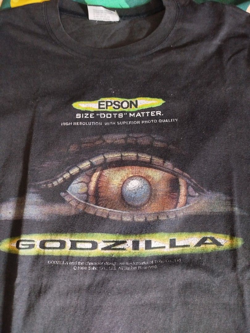 Godzilla Epson T-shirt vintage (Category: Tshirts & Polo Shirts ) located in Quezon City. Submitted by andreialej28522 (Listing ID 1426475240, Image 3). Description: Black Godzilla T-shirt featuring an Epson logo and eye graphic. The shirt has a crew neck and short sleeves. The Godzilla logo is printed on the front. The shirt is likely a promotional item for Epson. The shirt has a tag with the Godzilla logo..