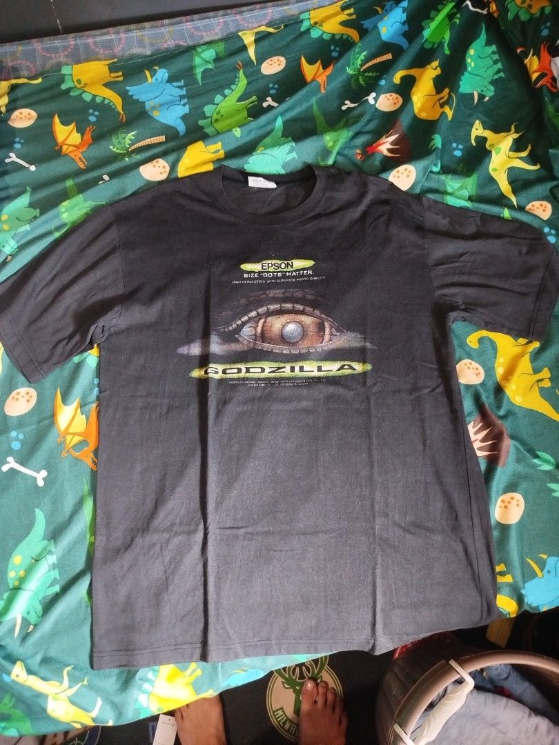 Godzilla Epson T-shirt vintage (Category: Tshirts & Polo Shirts ) located in Quezon City. Submitted by andreialej28522 (Listing ID 1426475240, Image 2). Description: Black Godzilla T-shirt featuring an Epson logo and eye graphic. The shirt has a crew neck and short sleeves. The Godzilla logo is printed on the front. The shirt is likely a promotional item for Epson. The shirt has a tag with the Godzilla logo..