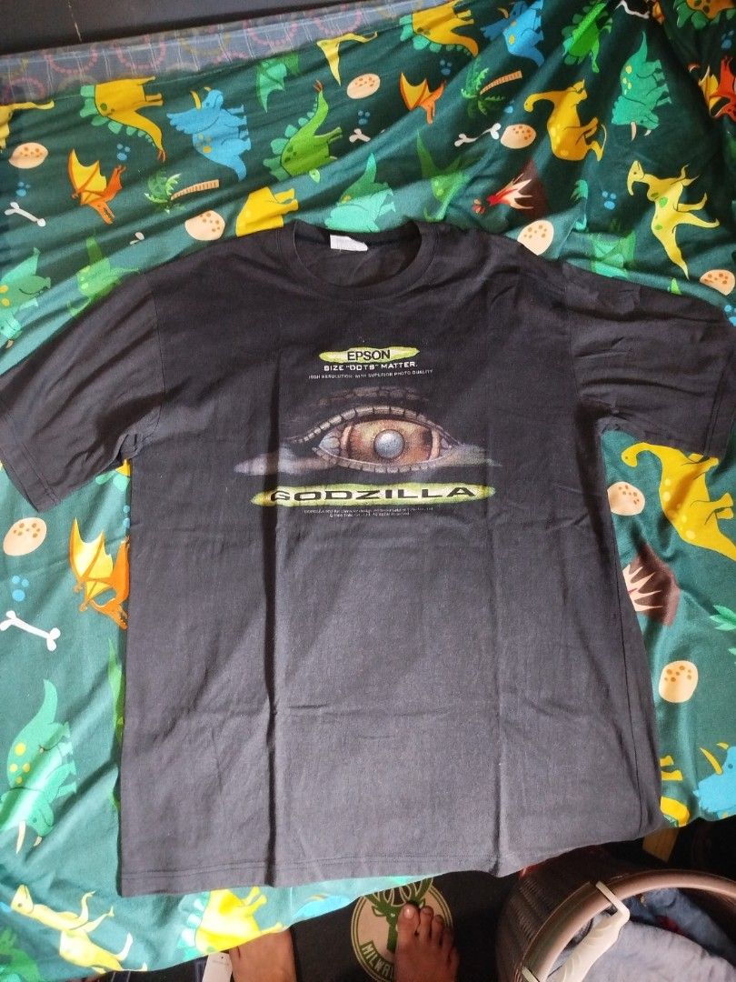 Godzilla Epson T-shirt vintage (Category: Tshirts & Polo Shirts ) located in Quezon City. Submitted by andreialej28522 (Listing ID 1426475240, Image 1). Description: Black Godzilla T-shirt featuring an Epson logo and eye graphic. The shirt has a crew neck and short sleeves. The Godzilla logo is printed on the front. The shirt is likely a promotional item for Epson. The shirt has a tag with the Godzilla logo..