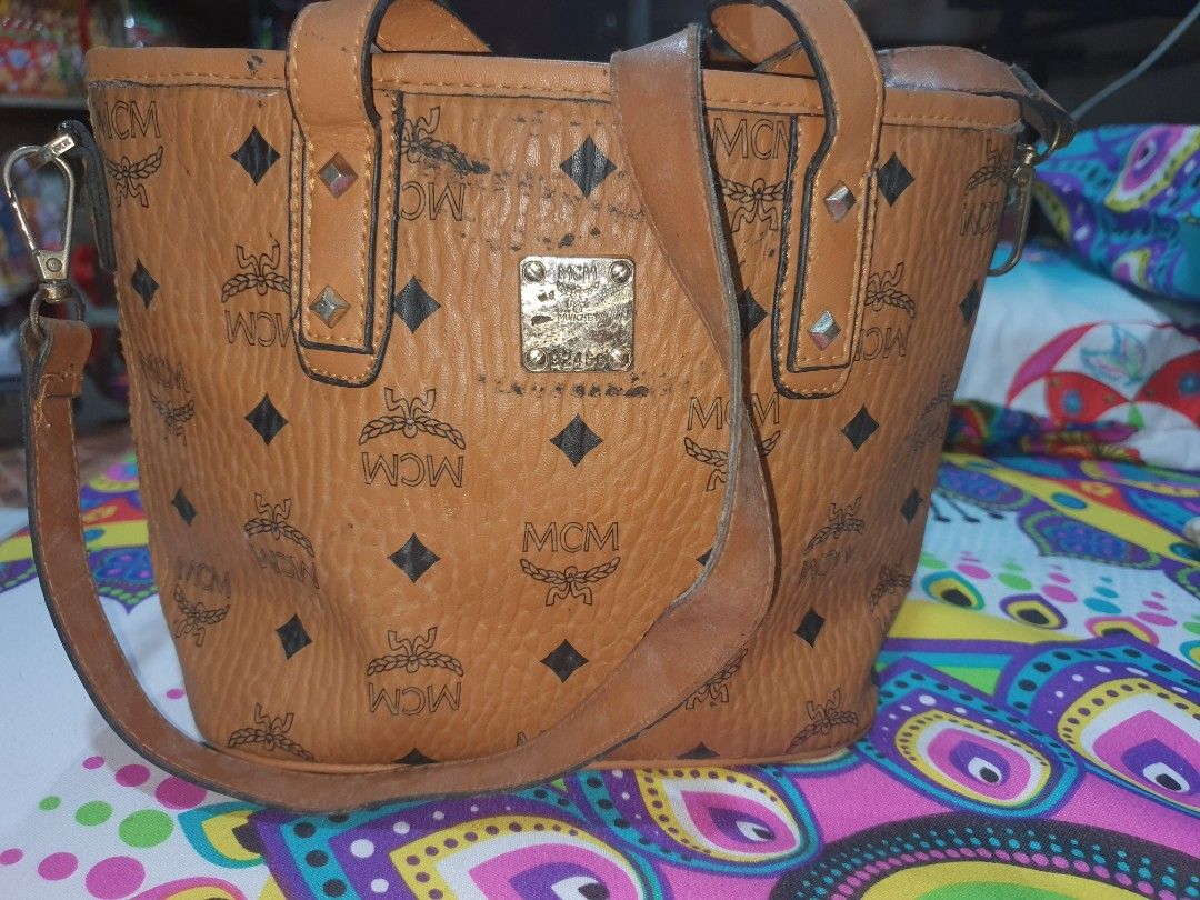 MCM Brown Tote Bag (Category: Luxury Bags & Wallets) located in Manila. Submitted by jemiclat3076761 (Listing ID 1426551901, Image 2). Description: MCM tote bag features a brown exterior with the brand's logo pattern. It has a top handle and a detachable shoulder strap. The bag includes a small metal plate with the MCM logo. The bag has some signs of wear..