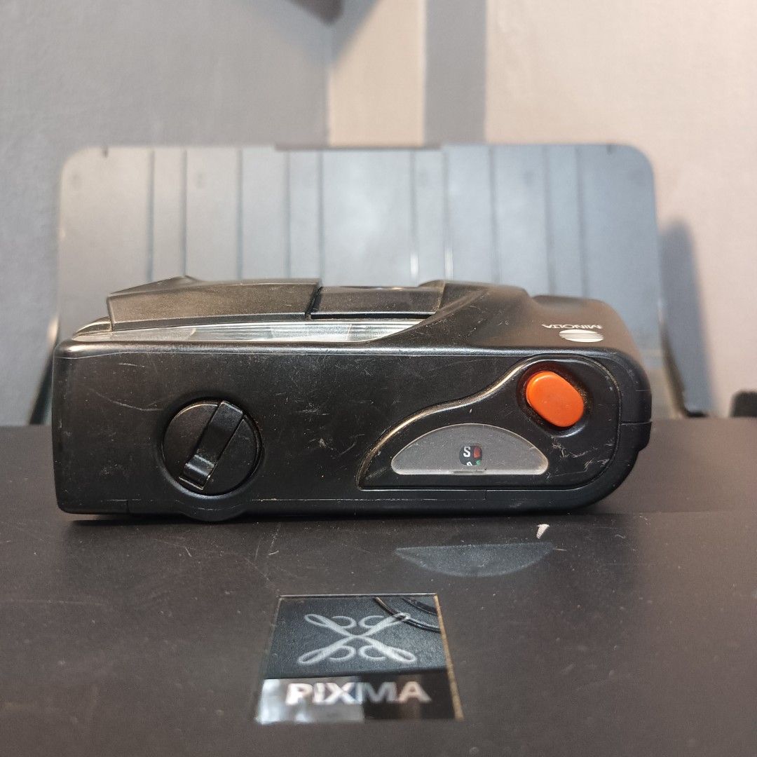 Minolta Memory Maker Film Camera (Category: Cameras) located in Caloocan City. Submitted by glavesart (Listing ID 1426432299, Image 3). Description: Minolta Memory Maker film camera. Features a built-in flash and a lens. The camera has a black body with an orange button. The camera's film compartment is accessible. Made in Malaysia. Includes instructions on the bottom of the camera..