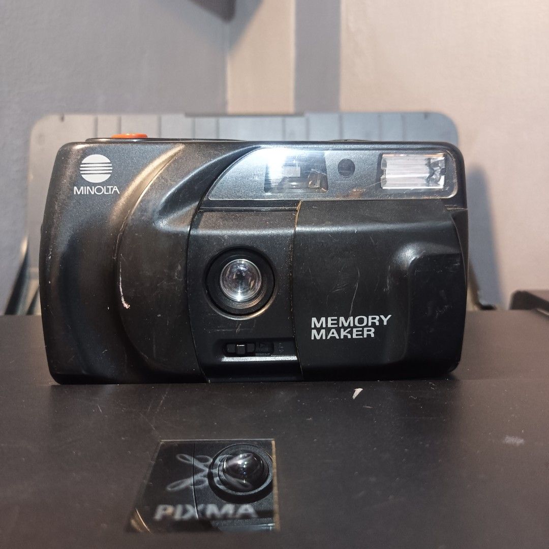 Minolta Memory Maker Film Camera (Category: Cameras) located in Caloocan City. Submitted by glavesart (Listing ID 1426432299, Image 1). Description: Minolta Memory Maker film camera. Features a built-in flash and a lens. The camera has a black body with an orange button. The camera's film compartment is accessible. Made in Malaysia. Includes instructions on the bottom of the camera..