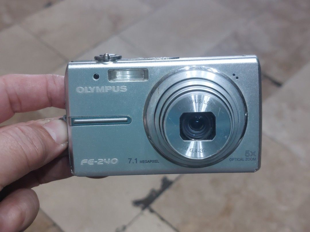 Olympus FE-240 Digital Camera (Category: Cameras) located in Manila. Submitted by jonrick.co (Listing ID 1426469138, Image 1). Description: Olympus FE-240 digital camera with 7.1 megapixels and 5x optical zoom. Features a silver body with a built-in flash and a display screen. Includes various buttons for menu, zoom, and mode selection. The camera shows a preview of a photo on the screen. slight issue may lines sa lcd pag ginagamit but wont affec