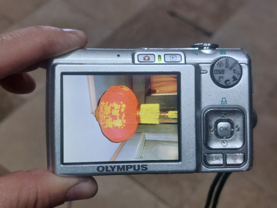 Olympus FE-240 Digital Camera (Category: Cameras) located in Manila. Submitted by jonrick.co (Listing ID 1426469138, Image 2). Description: Olympus FE-240 digital camera with 7.1 megapixels and 5x optical zoom. Features a silver body with a built-in flash and a display screen. Includes various buttons for menu, zoom, and mode selection. The camera shows a preview of a photo on the screen. slight issue may lines sa lcd pag ginagamit but wont affec