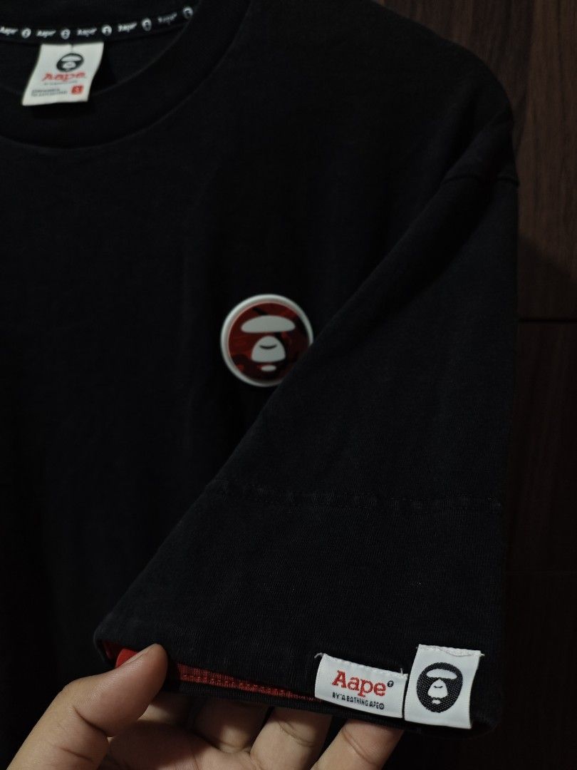 Aape by A Bathing Ape Black T-shirt (Category: Tshirts & Polo Shirts ) located in Borongan. Submitted by thrifthappens.ph (Listing ID 1426679174, Image 3). Description: Black Aape by A Bathing Ape T-shirt with a red camo hem. Features the Aape logo on the chest and sleeve. The tag indicates the size is S. Made of 100% cotton. The shirt has a crew neck and short sleeves. Aape Rubber Logo Shirt Excellent Condition Size S on tag Dimes: 22x27.5 Color