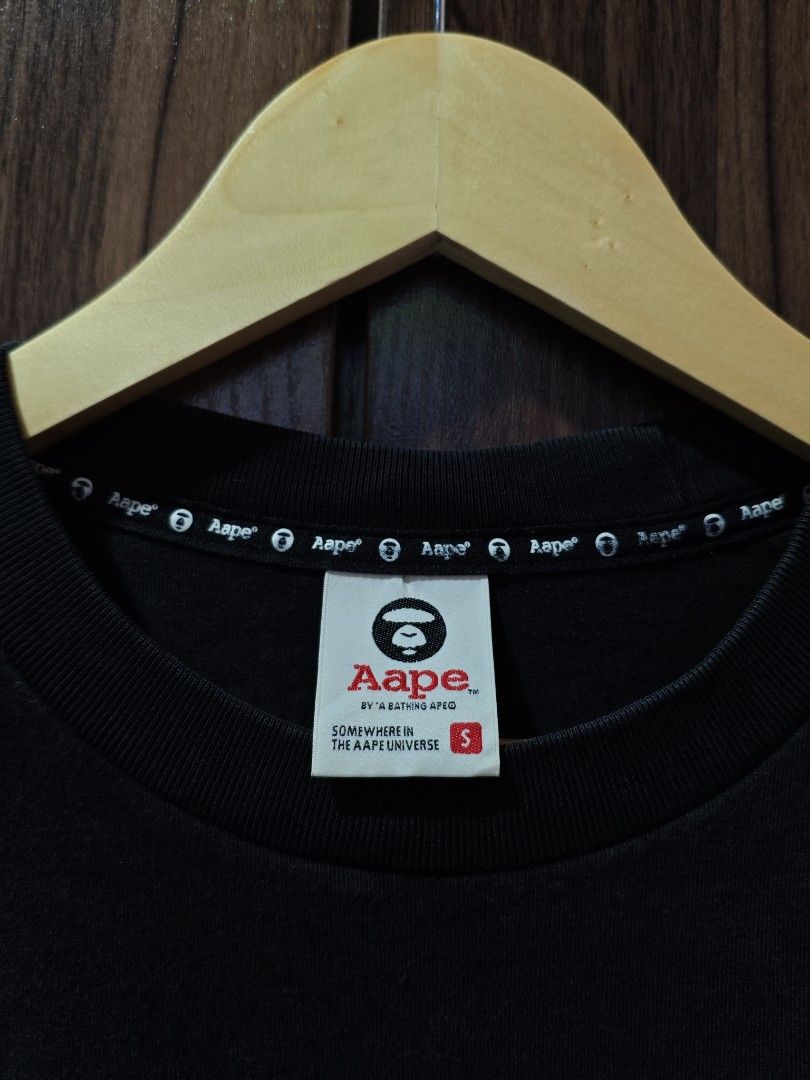 Aape by A Bathing Ape Black T-shirt (Category: Tshirts & Polo Shirts ) located in Borongan. Submitted by thrifthappens.ph (Listing ID 1426679174, Image 2). Description: Black Aape by A Bathing Ape T-shirt with a red camo hem. Features the Aape logo on the chest and sleeve. The tag indicates the size is S. Made of 100% cotton. The shirt has a crew neck and short sleeves. Aape Rubber Logo Shirt Excellent Condition Size S on tag Dimes: 22x27.5 Color