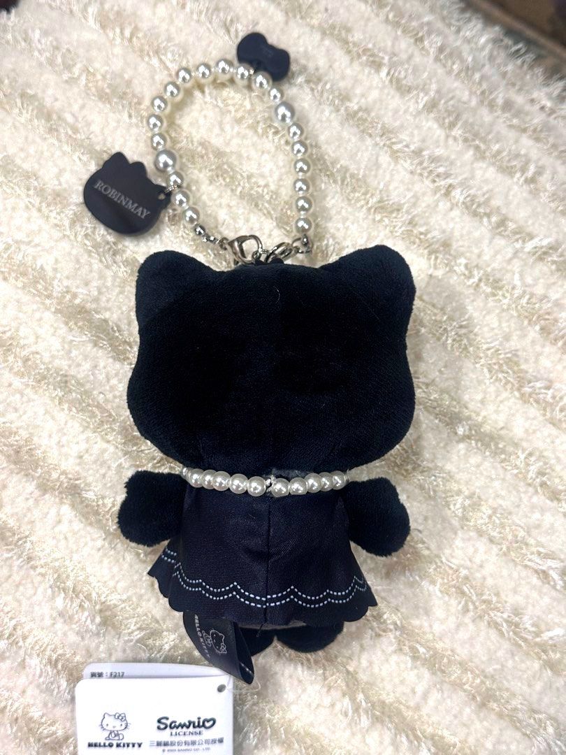Authentic Sanrio Hello Kitty x Robinmay Black Plush Charm (Category: Plushies & Soft Toys) located in Manila. Submitted by mybeadshop (Listing ID 1426775472, Image 2). Description: Kitty plush charm features a black design with a pearl necklace and a matching bow. It includes a pearl beaded strap and a Kitty tag. The plushie is wearing a black dress with a scalloped hemline. The back of the plushie shows the Robinmay tag..