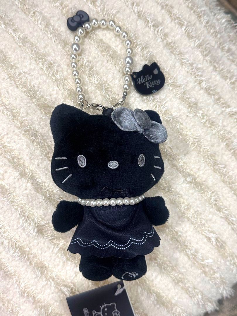 Authentic Sanrio Hello Kitty x Robinmay Black Plush Charm (Category: Plushies & Soft Toys) located in Manila. Submitted by mybeadshop (Listing ID 1426775472, Image 1). Description: Kitty plush charm features a black design with a pearl necklace and a matching bow. It includes a pearl beaded strap and a Kitty tag. The plushie is wearing a black dress with a scalloped hemline. The back of the plushie shows the Robinmay tag..