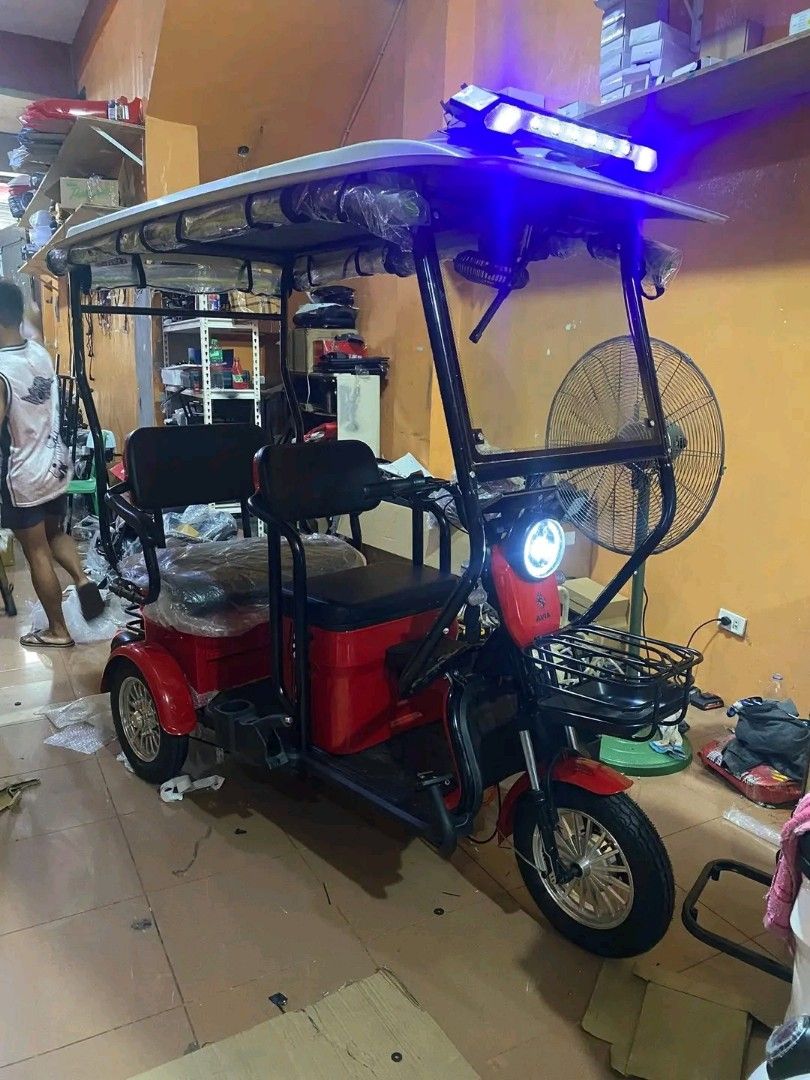 Electric Tricycle with Canopy (Category: Motorbikes for Sale) located in Manila. Submitted by saguittarian06 (Listing ID 1426687914, Image 2). Description: Electric tricycle with a canopy, designed for passenger transport. Features a front basket, headlights, and a rear cargo area. Available in multiple colors, including red, light blue, and white. Includes seating for multiple passengers. Equipped with lights on the canopy. ONHAND NA ANG BUDGET 