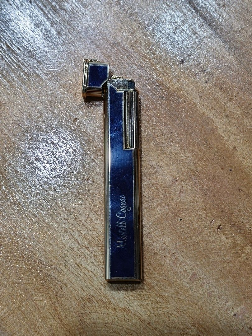 Martell Cognac Lighter (Category: Vintage Collectibles) located in Candon. Submitted by ylocos_thrifts (Listing ID 1426748571, Image 2). Description: Vintage lighter featuring the Martell Cognac branding. It has a rectangular shape with a gold-colored frame and a blue center. The lighter is marked with the "Martell Cognac" logo in a cursive font. The images show the lighter in both open and closed positions..