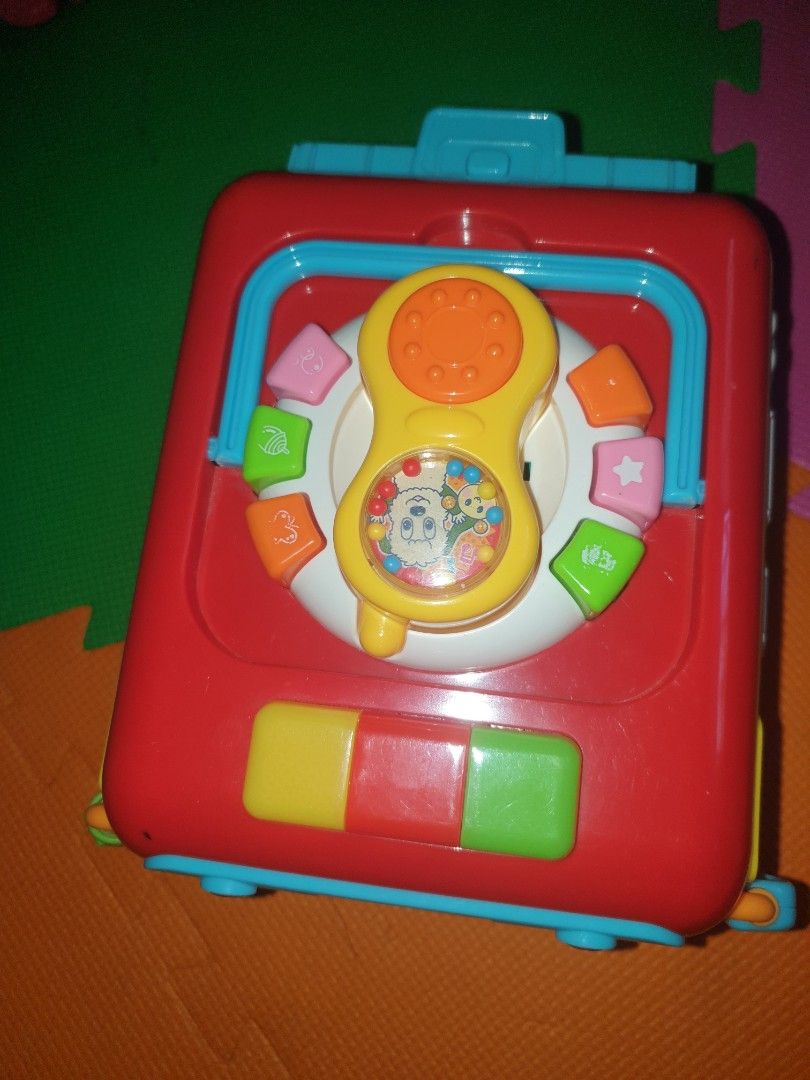 wanwan&u-tan musical busy bus (Category: Infant Playtime) located in Quezon City. Submitted by krmariam13 (Listing ID 1426599061, Image 3). Description: Colorful musical activity cube toy features various interactive elements, including buttons, gears, and shape sorters. It has a bus design with cartoon characters and lights. It also has a handle for easy carrying..