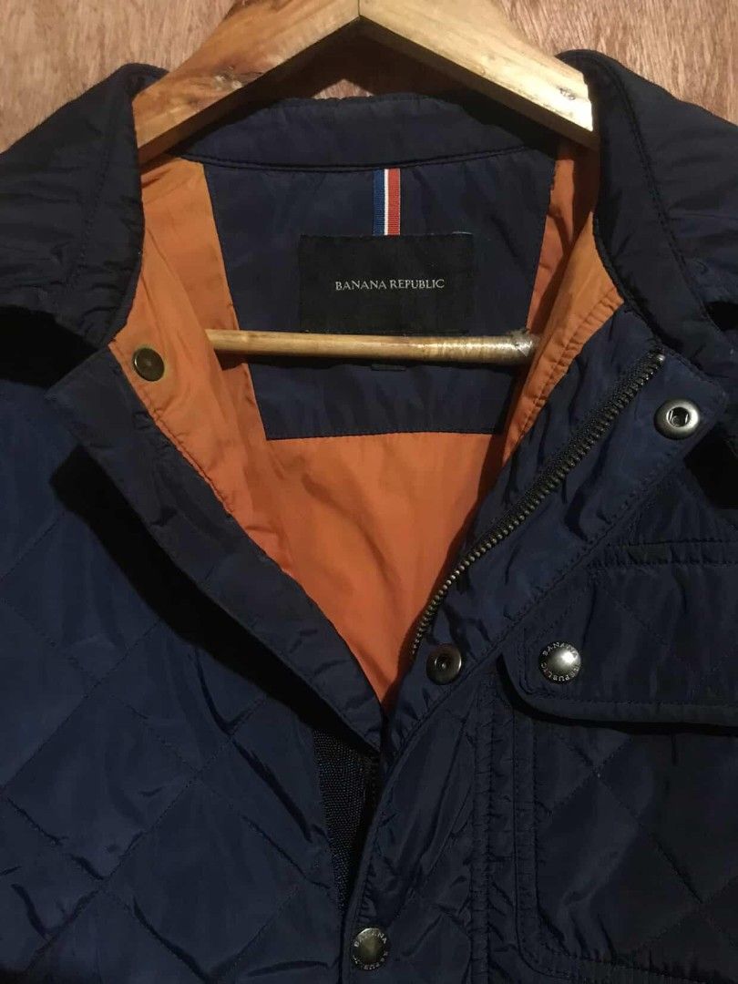 Banana Republic Quilted Jacket (Category: Coats, Jackets and Outerwear) located in Manila. Submitted by ronmark (Listing ID 1426815592, Image 2). Description: Navy blue quilted jacket from Banana Republic. Features an orange lining and button closure. Includes two front pockets and a zippered pocket. The jacket has the Banana Republic logo on the buttons. Made of 100% polyester..