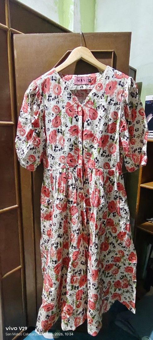 Floral Print Dress (Category: Dresses) located in Quezon City. Submitted by ak_0406 (Listing ID 1426871465, Image 1). Description: Dress features a beautiful floral print with red and pink flowers on a white background. It has a V-neckline and short sleeves. The dress has a gathered waist and a flowy skirt. The dress is hanging on a wooden hanger..