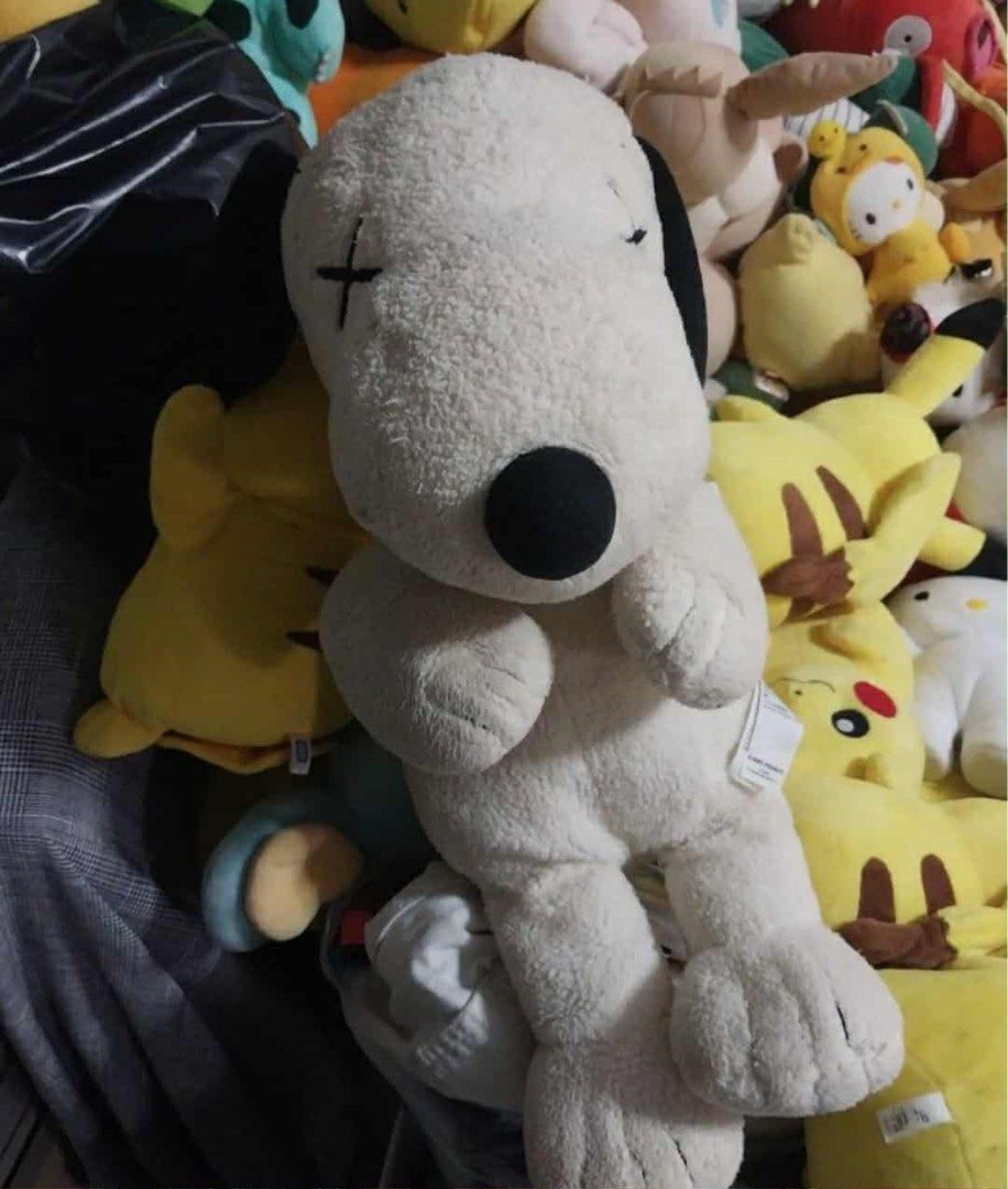 KAWS x Peanuts Snoopy Plush Toy (Category: Plushies & Soft Toys) located in Manila. Submitted by kuya_moto (Listing ID 1427056174, Image 3). Description: KAWS x Peanuts Snoopy plush toy features a cream-colored body with black ears and a black nose. It has the signature KAWS "X" eyes and a red collar. The tag indicates it is made in China with polyester fiber. It is a medium-sized plush toy..