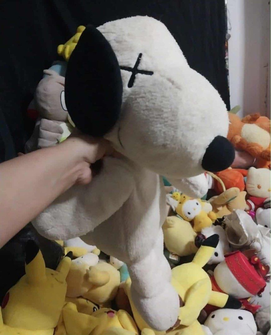 KAWS x Peanuts Snoopy Plush Toy (Category: Plushies & Soft Toys) located in Manila. Submitted by kuya_moto (Listing ID 1427056174, Image 2). Description: KAWS x Peanuts Snoopy plush toy features a cream-colored body with black ears and a black nose. It has the signature KAWS "X" eyes and a red collar. The tag indicates it is made in China with polyester fiber. It is a medium-sized plush toy..