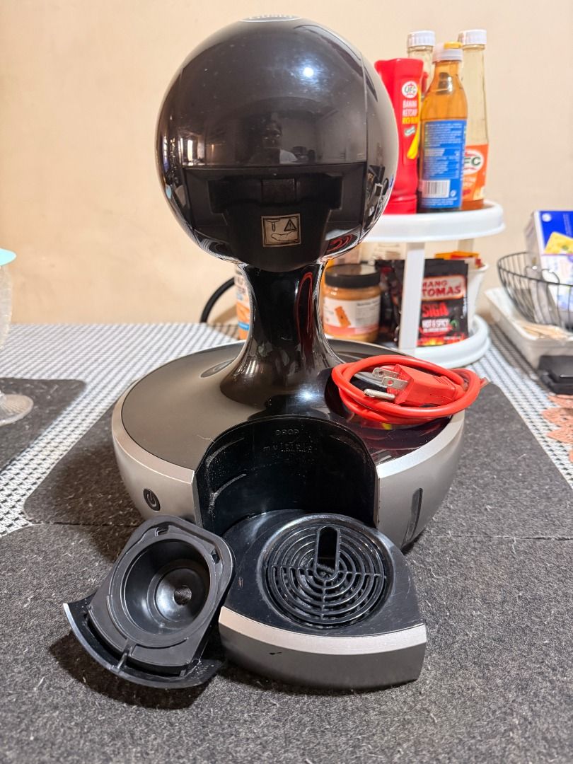 Nescafe Dolce Gusto Coffee Machine (Category: Coffee Machines & Makers) located in Quezon City. Submitted by raindr0ps12 (Listing ID 1427038407, Image 3). Description: Nescafe Dolce Gusto automatic coffee machine with with height-adjustable drip tray. Features a black and silver design with a round top. Includes the main unit, a removable capsule holder, and a power cord. Perfect for making your favorite hot or cold coffee drinks at home. with si
