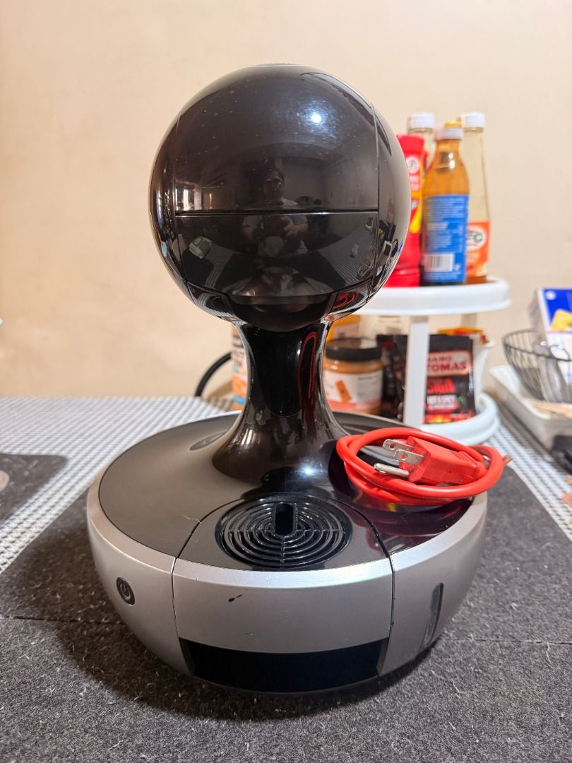 Nescafe Dolce Gusto Coffee Machine (Category: Coffee Machines & Makers) located in Quezon City. Submitted by raindr0ps12 (Listing ID 1427038407, Image 2). Description: Nescafe Dolce Gusto automatic coffee machine with with height-adjustable drip tray. Features a black and silver design with a round top. Includes the main unit, a removable capsule holder, and a power cord. Perfect for making your favorite hot or cold coffee drinks at home. with si