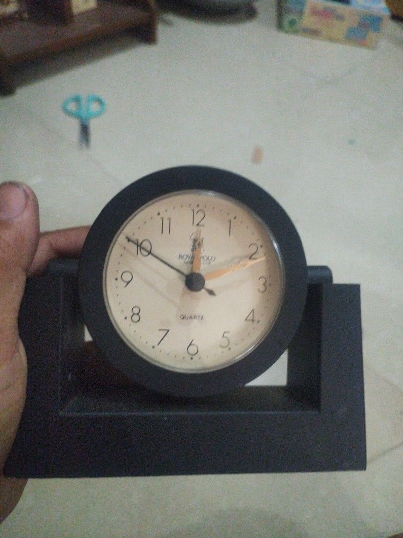 Branded Royal polo Quartz Table Clock (Category: Clocks) located in San Rafael. Submitted by jflshoppe1989 (Listing ID 1427231846, Image 1). Description: Black Acme Quartz table clock. It has a round clock face with a cream-colored background and black numbers. The clock has a black rectangular base. The clock hands are black and orange. The clock is in good working condition..