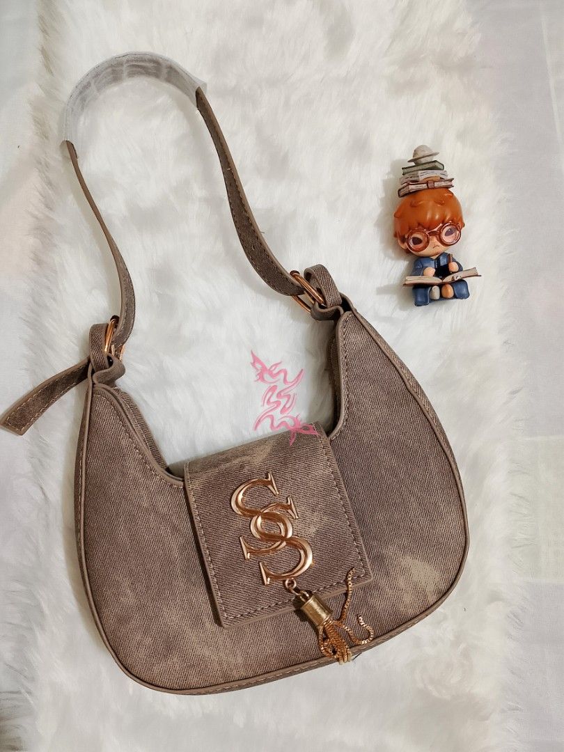 Shoulder Bag with Gold Accents (Category: Shoulder Bags) located in Manila. Submitted by dala.collection (Listing ID 1427226248, Image 1). Description: Stylish shoulder bag in a neutral color. Features a flap closure with gold-colored hardware and a decorative charm. The bag has a single shoulder strap. The bag is set against a white, fluffy background..