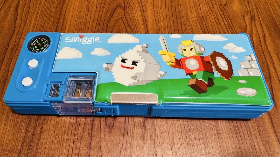 Smiggle Pixelated Pencil Case with Compass (Category: Stationery & School Supplies) located in Singapore. Submitted by anny66 (Listing ID 1427237245, Image 1). Description: Fun Smiggle pencil case featuring a pixelated design with a compass and pencil sharpener. It has a few compartments for storing stationery. Perfect for school or creative projects!.