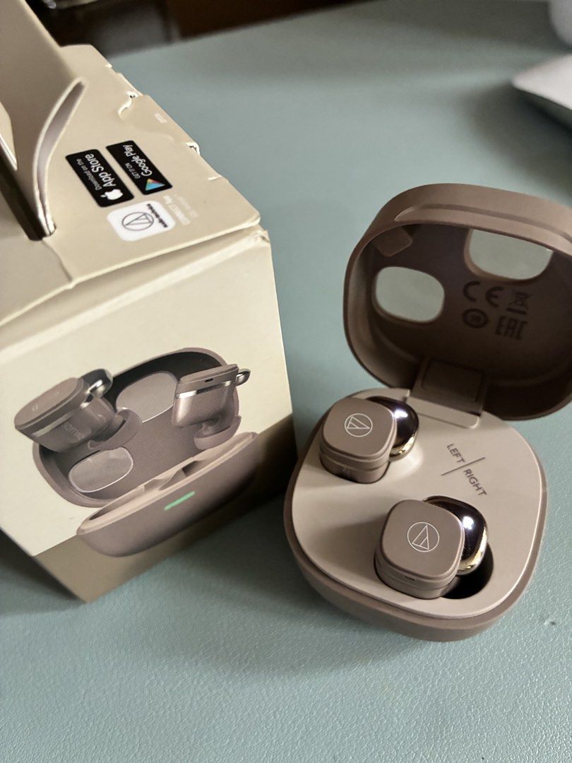 Audio-Technica ATH-S011TW2 Wireless Earbuds (Category: Earphones) located in Makati City. Submitted by dailyticker (Listing ID 1427365134, Image 1). Description: Audio-Technica ATH-S011TW2 wireless earbuds. Comes with the original box. The charging case and earbuds are in a tan color. The case has a 'Left' and 'Right' indicator. The box shows the earbuds and case. The box also indicates compatibility with the App Store and Google Play. Used only 