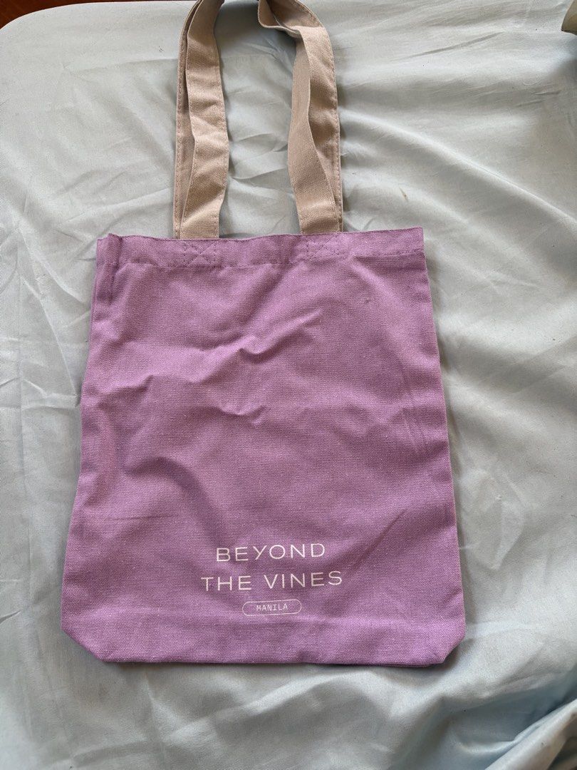 Beyond The Vines Manila Tote Bag small (Category: Tote Bags) located in Quezon City. Submitted by brandedthingsforless (Listing ID 1427482946, Image 1). Description: Beyond The Vines tote bag is made of purple fabric with beige handles. It features the brand's logo on the front and some text on the back. The bag is designed with the phrase "GOOD DESIGN ACCESSIBLE TO ALL" on the back. It is a simple and stylish bag suitable for everyday use..