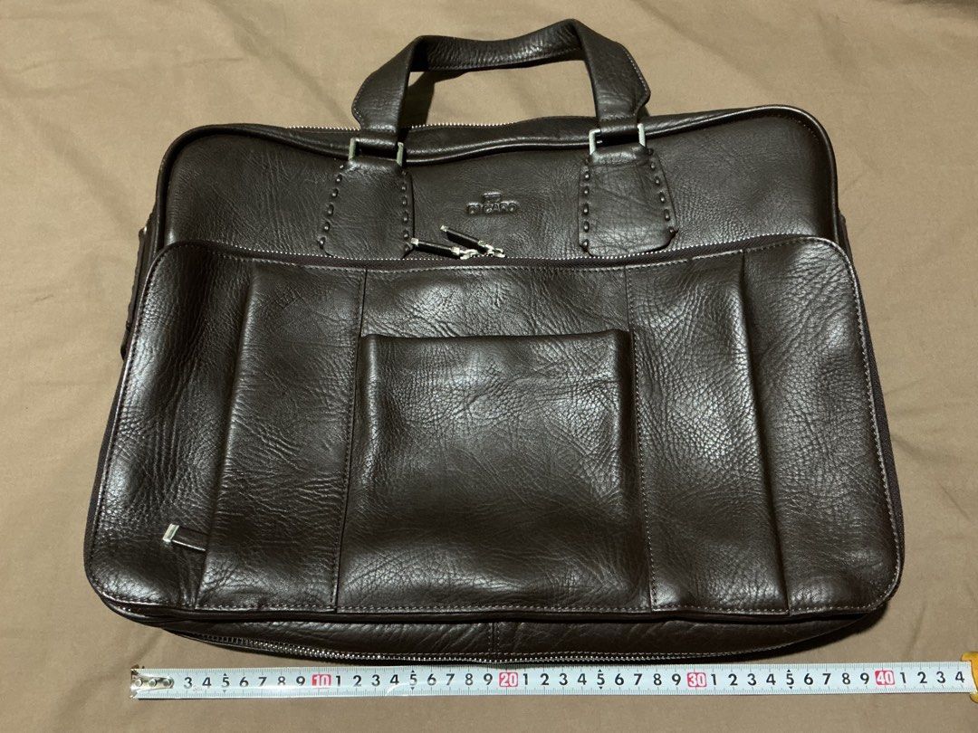 Di Caro Brown Leather Briefcase (Category: Luxury Bags & Wallets) located in Angeles City. Submitted by goodbuysathome (Listing ID 1427432917, Image 1). Description: Di Caro briefcase is made of brown leather. It features a top handle, multiple zippered compartments, and a front pocket. The interior has several pockets and compartments for organization. The bag has a silver-tone zipper and hardware. The brand name is visible on the front and insi