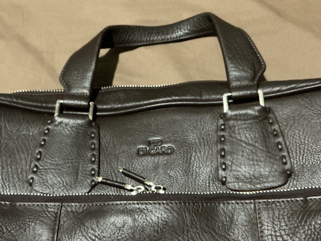 Di Caro Brown Leather Briefcase (Category: Luxury Bags & Wallets) located in Angeles City. Submitted by goodbuysathome (Listing ID 1427432917, Image 2). Description: Di Caro briefcase is made of brown leather. It features a top handle, multiple zippered compartments, and a front pocket. The interior has several pockets and compartments for organization. The bag has a silver-tone zipper and hardware. The brand name is visible on the front and insi