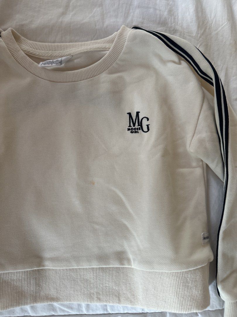 Moose Girl Sweatshirt - Size 8 (Category: Babies & Kids Fashion) located in Muntinlupa City. Submitted by shopnb (Listing ID 1427383169, Image 2). Description: Cream-colored sweatshirt from Moon Girl with black stripes on the sleeves. Features the "MG Moon Girl" logo on the front. It has a ribbed hem and cuffs. The size tag indicates size 8..
