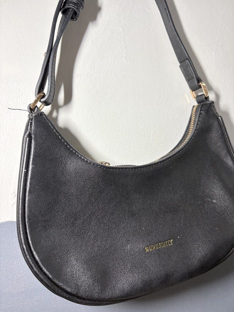Mumuselect Black Shoulder Bag (Category: Shoulder Bags) located in Rizal. Submitted by juliakejdn (Listing ID 1427484403, Image 3). Description: Black shoulder bag from Mumuselect. Features a crescent shape with a zipper closure. The bag has a single shoulder strap and a gold-colored zipper. The interior is lined with a light-colored fabric and includes a small pocket. The exterior has the brand name in gold lettering..