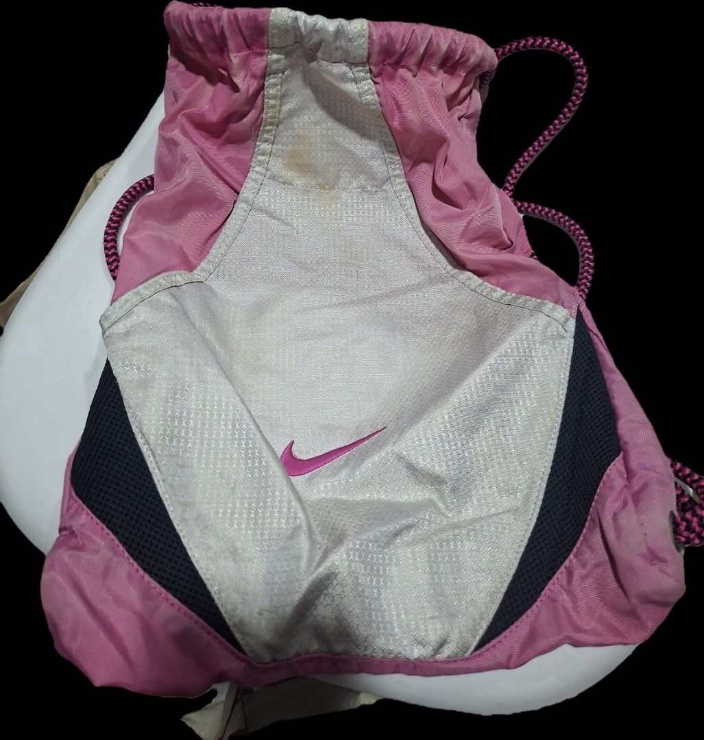 Nike Drawstring Bag with Interior Pockets (Category: Backpacks) located in Paranaque City. Submitted by potatoiceblended (Listing ID 1427394732, Image 1). Description: Pink Nike drawstring bag. Features a main compartment with a drawstring closure and two interior zippered pockets. The bag has a pink and silver color scheme with the Nike logo in pink. The straps are pink and black. The interior lining has a plaid pattern. issue: madumi.