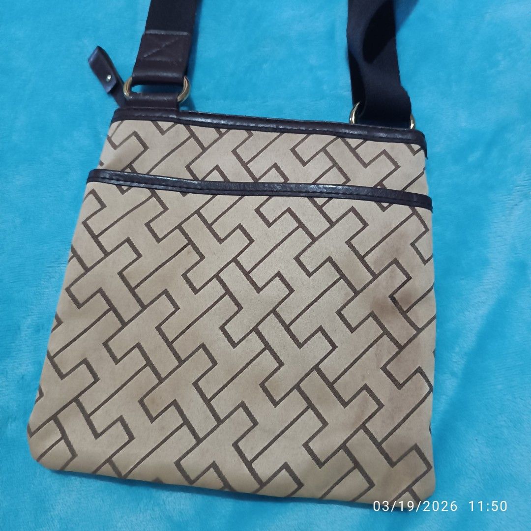 Tommy Hilfiger Crossbody Bag (Category: Cross-body Bags) located in Bacoor. Submitted by pamelott (Listing ID 1427337282, Image 3). Description: This is a Tommy Hilfiger crossbody bag featuring a classic, preppy design. ​Monogram Print: The body of the bag is covered in a geometric "T" monogram pattern in a dark brown/tan color scheme. ​Center Stripe: A bold, vertical canvas stripe runs down the center of the bag, consisting of dark chocolate bro