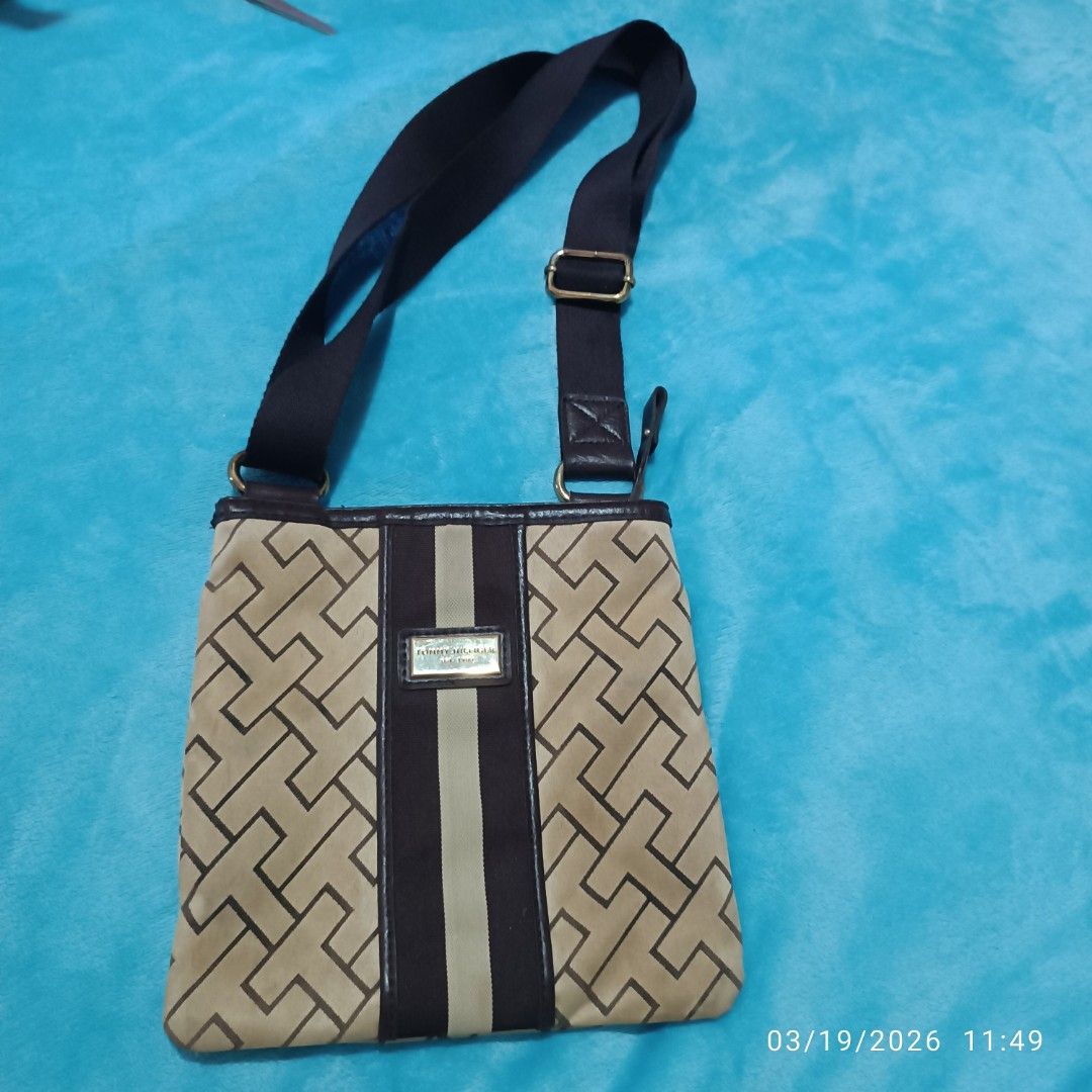 Tommy Hilfiger Crossbody Bag (Category: Cross-body Bags) located in Bacoor. Submitted by pamelott (Listing ID 1427337282, Image 1). Description: This is a Tommy Hilfiger crossbody bag featuring a classic, preppy design. ​Monogram Print: The body of the bag is covered in a geometric "T" monogram pattern in a dark brown/tan color scheme. ​Center Stripe: A bold, vertical canvas stripe runs down the center of the bag, consisting of dark chocolate bro
