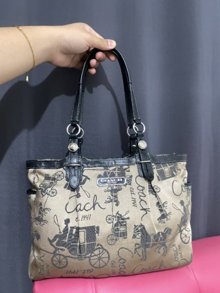 Coach Tote Bag with Carriage Print (Category: Luxury Bags & Wallets) located in Caloocan City. Submitted by cessang24 (Listing ID 1424323057, Image 1). Description: Coach tote bag featuring a classic carriage print. It has black leather handles and trim, with silver hardware accents. The bag has a beige background with a repeating pattern of carriages and the Coach logo..
