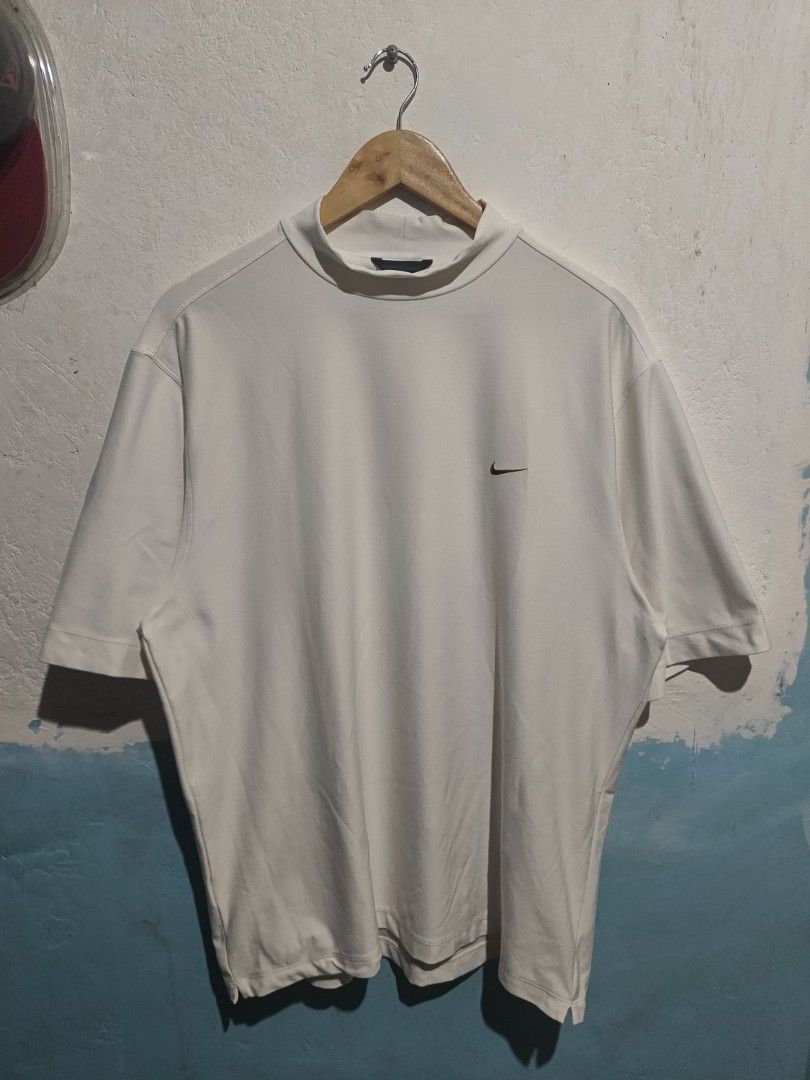 Nike Golf Mock Neck T-Shirt (Category: Tshirts & Polo Shirts ) located in Caloocan City. Submitted by mstrpreloved (Listing ID 1424316093, Image 1). Description: White Nike Golf mock neck t-shirt. Features a small Nike logo on the chest. The shirt has a mock neck collar and short sleeves. The tag indicates it is a men's shirt. Made in China..