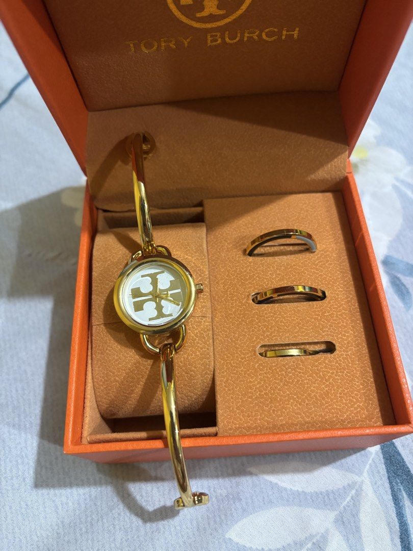 Tory Burch Ladies Bangle Watch with Rings (Category: Women's Watches) located in Manila. Submitted by elizabeth-declutter (Listing ID 1424168100, Image 1). Description: - Tory Burch ladies watch and ring set. - Gold-tone bracelet. - White dial with Tory Burch logo. - Includes three matching rings. - Comes with original orange box. - Perfect for a sophisticated look..
