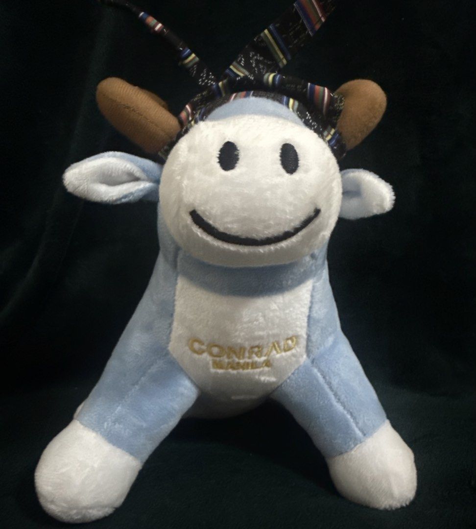 Conrad Manila Plush Cow (Category: Plushies & Soft Toys) located in Pasay City. Submitted by addtocartacademy (Listing ID 1427614099, Image 2). Description: Adorable plush cow is from Conrad Manila. It features a light blue body with white accents on the face, feet, and tail. The cow has brown horns and a patterned headpiece. The Conrad Manila logo is embroidered on the chest. It's a cute and cuddly collectible item..