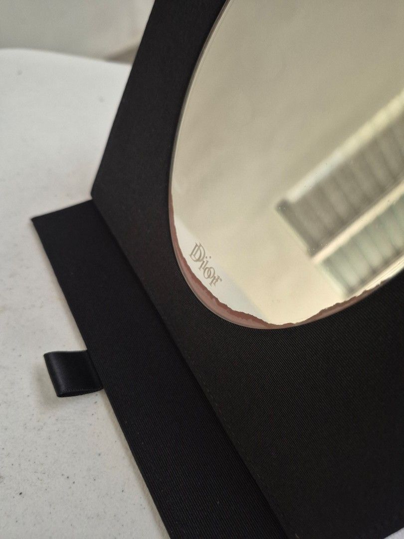 Dior Compact Mirror (Category: Mirrors) located in Santa Rosa. Submitted by thesecondshelf (Listing ID 1427569841, Image 2). Description: Dior compact mirror in a black case. The mirror has the Dior logo etched on it. The case is square-shaped and has a ribbon closure. The mirror is oval-shaped. Issue: mirror stain on the lower part. It still has its mirror protector. .