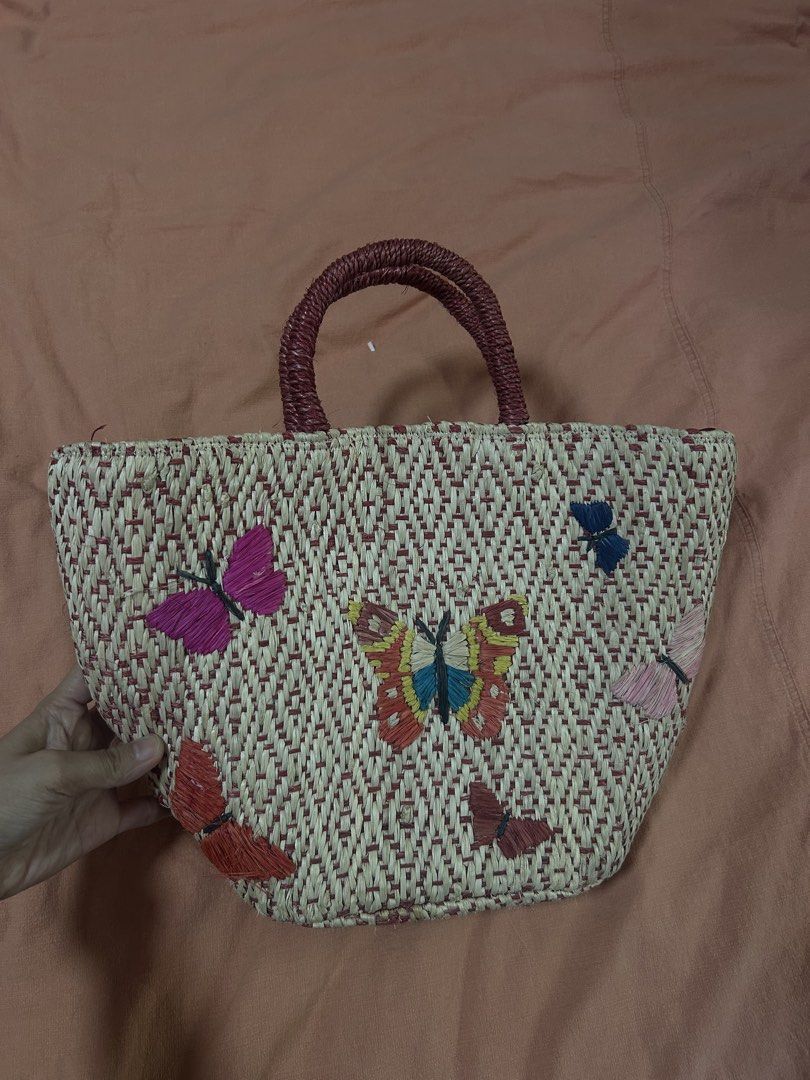 Embroidered Butterfly Straw Handbag (Category: Beach Bags) located in Manila. Submitted by treenitea (Listing ID 1427509107, Image 1). Description: Straw handbag features an intricate butterfly embroidery design. It has a woven texture with a red and beige color scheme. The bag includes a pair of handles and a drawstring closure. The interior is lined with a dark red fabric. It's a stylish accessory for everyday use..