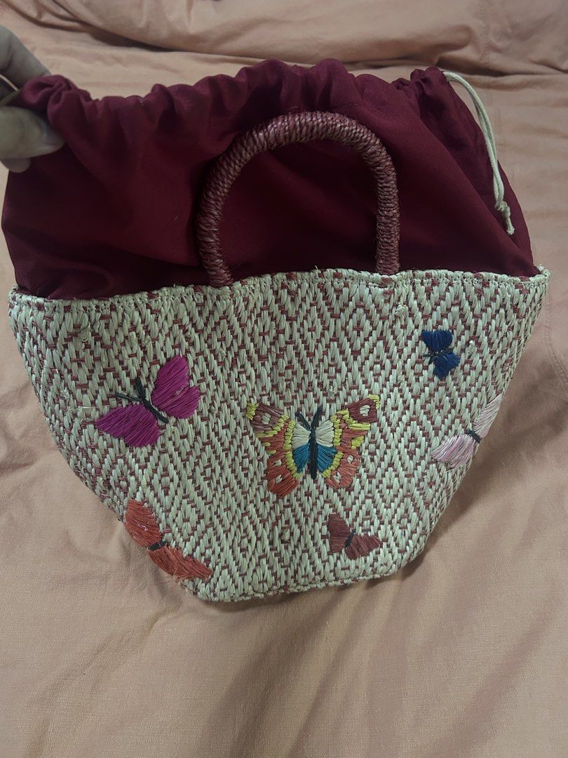 Embroidered Butterfly Straw Handbag (Category: Beach Bags) located in Manila. Submitted by treenitea (Listing ID 1427509107, Image 3). Description: Straw handbag features an intricate butterfly embroidery design. It has a woven texture with a red and beige color scheme. The bag includes a pair of handles and a drawstring closure. The interior is lined with a dark red fabric. It's a stylish accessory for everyday use..