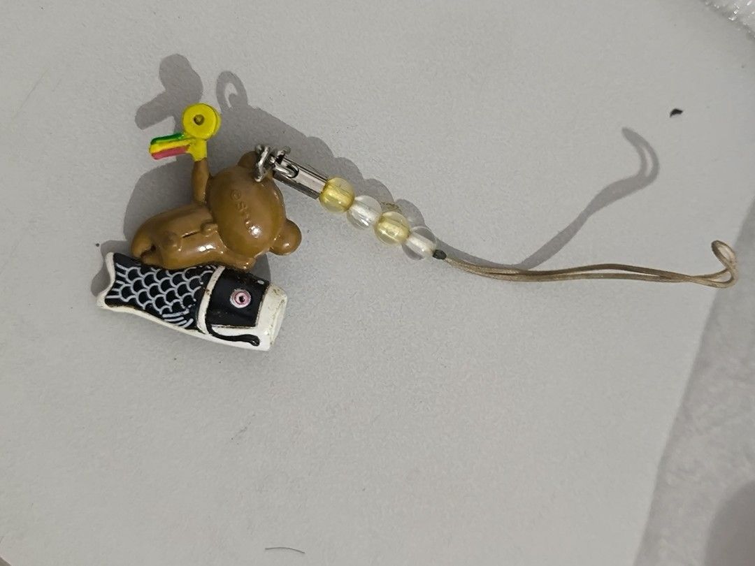 Japanese Bear and Fish Keychain (Category: Character Goods) located in Angeles City. Submitted by yellowbrickstore (Listing ID 1427612962, Image 2). Description: Adorable keychain features a brown bear riding on a fish. It has a string with beads and a hook for easy attachment. The keychain is likely made of metal and enamel. It's a cute accessory for bags, keys, or as a decorative item. The design is likely inspired by Japanese culture. shipping