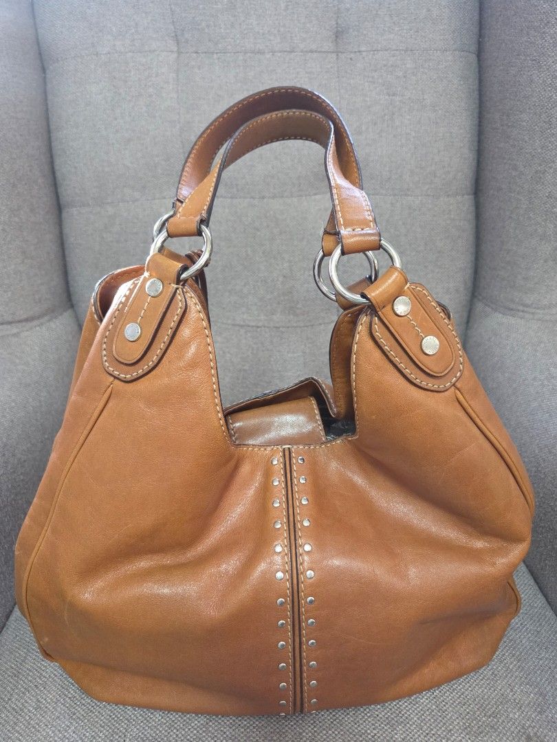 Michael Kors Leather Hobo Bag (Category: Luxury Bags & Wallets) located in Muntinlupa City. Submitted by cpar07 (Listing ID 1427637730, Image 2). Description: - Genuine leather Michael Kors hobo bag - Warm brown color - Silver MK logo charm - Studded details - Multiple interior compartments - Includes small attached wallet - Double shoulder straps - Silver hardware - MK logo patterned interior lining.