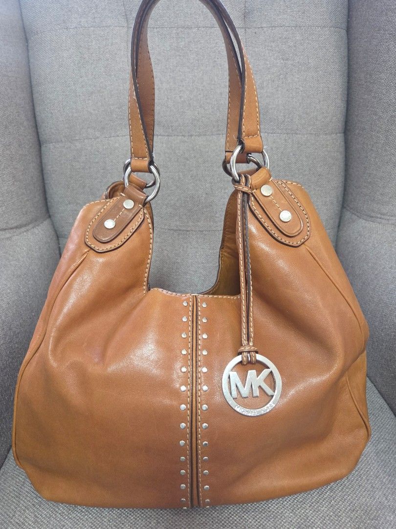 Michael Kors Leather Hobo Bag (Category: Luxury Bags & Wallets) located in Muntinlupa City. Submitted by cpar07 (Listing ID 1427637730, Image 1). Description: - Genuine leather Michael Kors hobo bag - Warm brown color - Silver MK logo charm - Studded details - Multiple interior compartments - Includes small attached wallet - Double shoulder straps - Silver hardware - MK logo patterned interior lining.